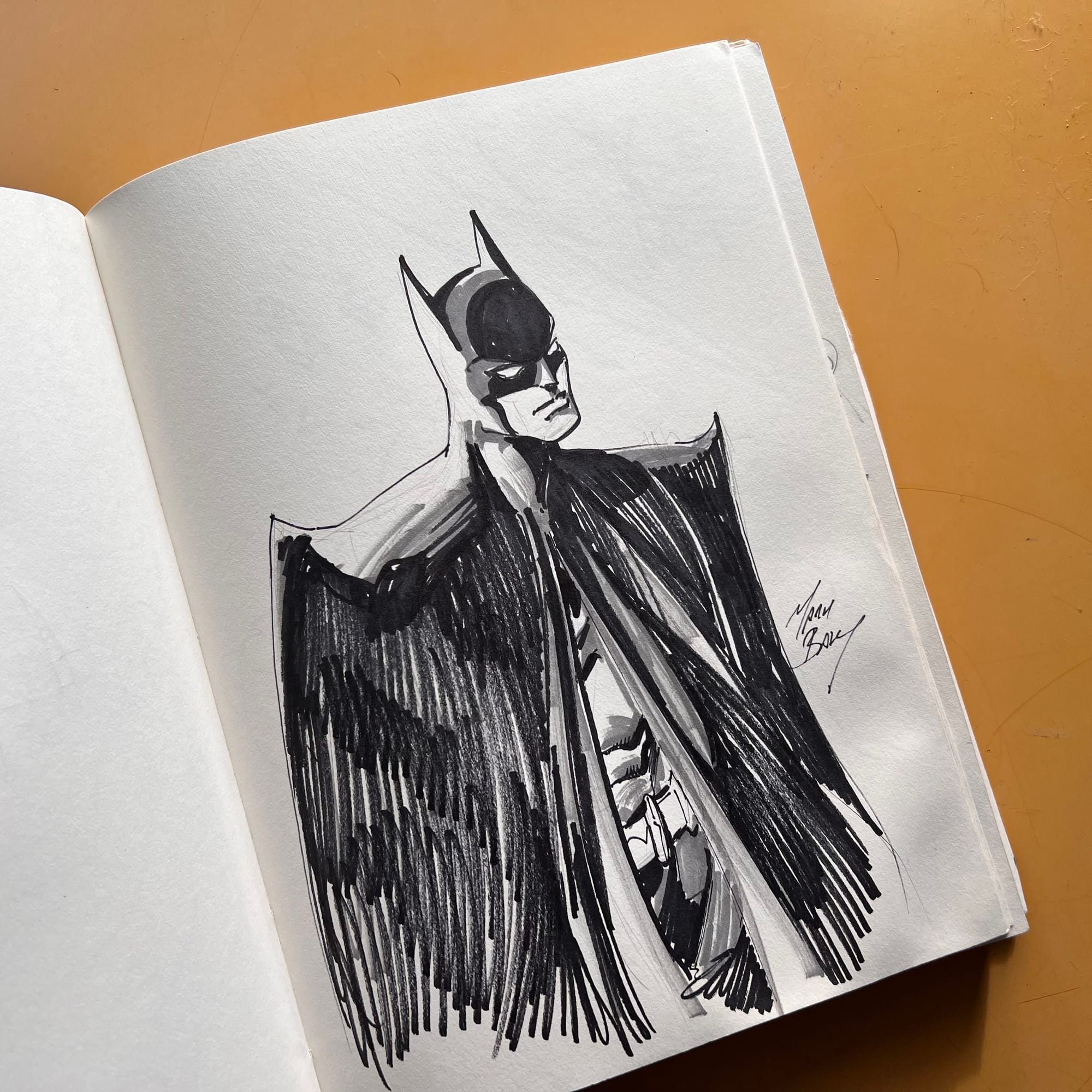 A marker drawing of Batman in black and white in a sketchbook by Mark Bagley